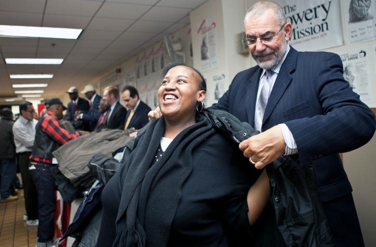 COAT DRIVE: A woman is assisted with a new coat by President and General Manager of WNBC Michael Jack at the Bowery Mission on Wednesday. The New York Cares annual coat drive began Wednesday.  (The Epoch Times)