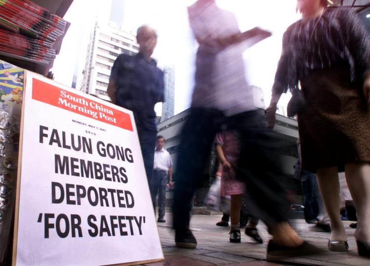 People walk past a newspaper headline announcing the deportation of two Falun Gong practitioners on a street in Hong Kong on May 7, 2001. (Peter Parks/AFP/Getty Images)