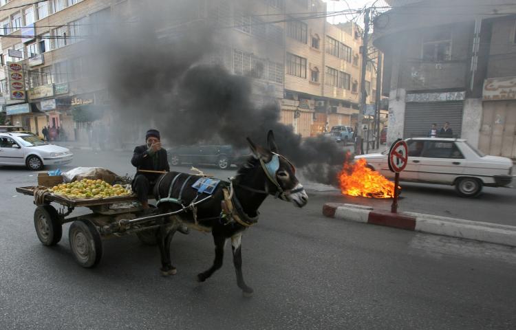 A Palestinian man rides on his donkey cart past burning tires in Gaza. A similar donkey-drawn wagon was rigged with an explosive device and detonated at the Gaza security fence on Tuesday morning.  (Mahmud Hams/Getty Images)