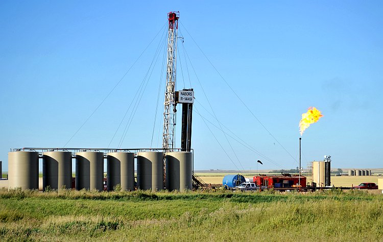 Natural gas is burned off next to an oil well being drilled by workers