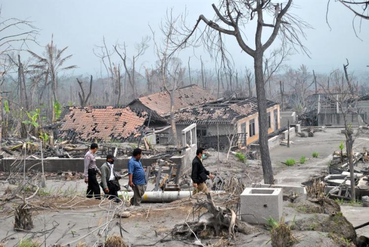 A villager (second right) is escorted by officials as he returns to assess the volcano damage in his village in Sleman District near Mount Merapi. (Wayan Manuh/The Epoch Times)