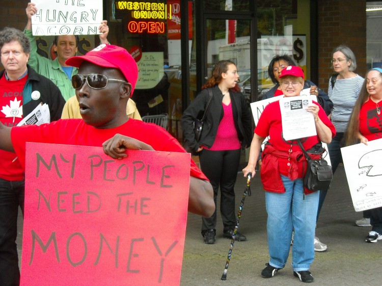 Pascal Apuwa (forefront) demonstrates with fellow ACORN members outside a Money Mart in Burnaby, B.C., against the unreasonably high fees placed on remittance payments by money transfer organizations.  (Acorn Canada)