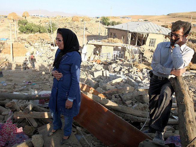 An Iranian man and woman stand on top of the rubble of their destroyed house in the village of Baje-Baj, near the town of Varzaqan, on August 12, 2012