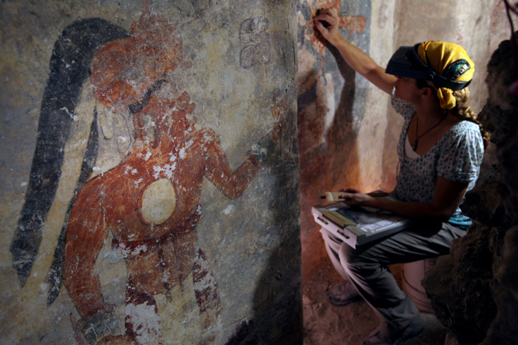 Conservator Angelyn Bass cleans and stabilizes the surface of a wall of a Maya house that dates to the 9th century A.D. The figure of a man who may have been the town scribe appears on the wall to her left. The research is supported by the National Geographic Society. (Tyrone Turner © 2012 National Geographic) 