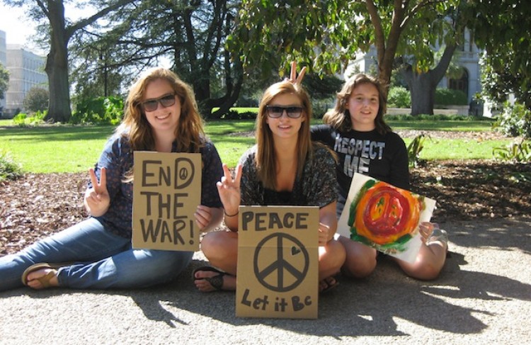 Sarah Rowl, Jenna Cooley, and Miranda Kinard hold up signs for peace and no wars. Cooley said she hopes for a better community. (Kelly Ni/The Epoch Times)