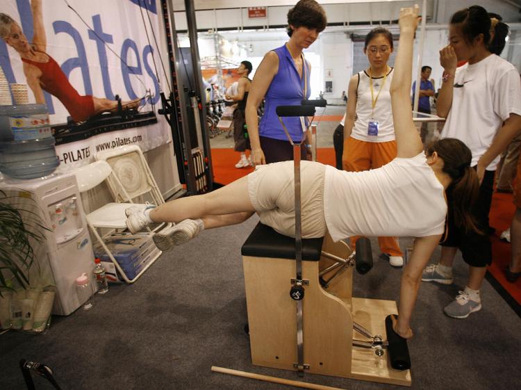 A woman tries working out on a Pilates exercise machine at the Fitness China Beijing 2006 expo in Beijing, 17 July 2006.  (Frederic J. Brown/AFP/Getty Images)