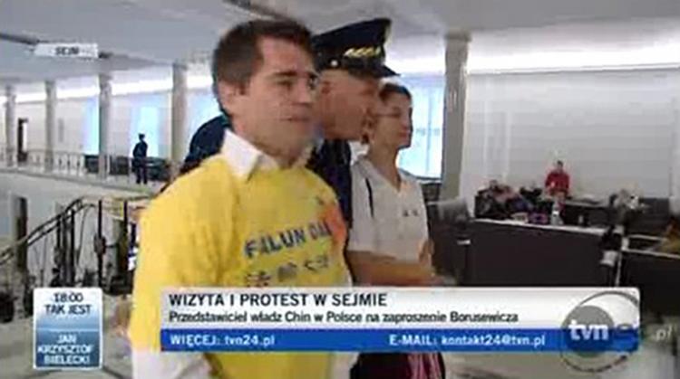 A screen shot from Polish TVP24 of the two protestors being escorted by a parliamentary security guard.  (Screenshot of TVP24)