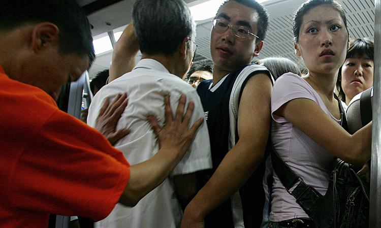 A subway worker (L) pushes commuters into a subway train in Beijing, China, an action that will not go over well with Western tourists next month.  (Guang Niu/Getty Images)
