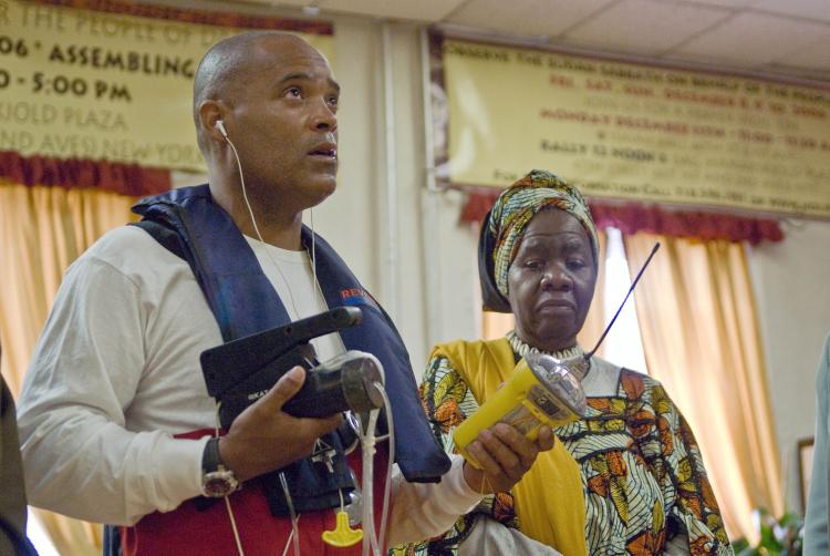 DIFFICULT JOURNEY: Victor Mooney (L) holds an emergency beacon in his left hand and a water-maker in his right hand. The Queen Mother Dr. Delois Blakely, the ambassador of Goodwill of Goree Island stands to his right. Mooney was forced to end his rowboat  (Joshuan Philipp/The Epoch Times)