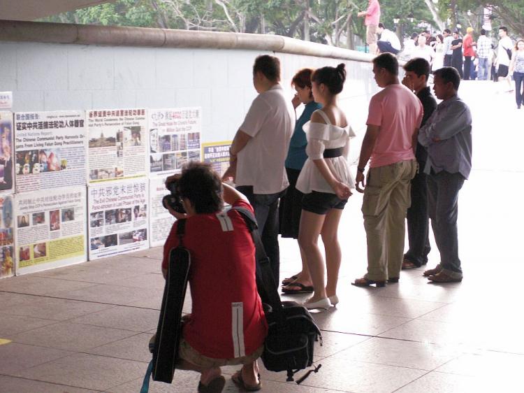 People read posters detailing the persecution of Falun Gong in China. The posters are at the walkway below Esplanade Bridge, in Esplanade Park, Singapore. (Mingguo Sun/The Epoch Times)