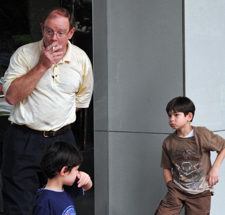 A man smokes a cigarette by children