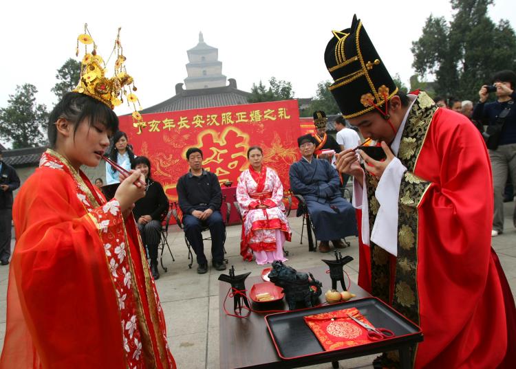 LINKED BY DESTINY: A newly wed couple dressed in traditional Han costumes drinks wine from a pair of cups linked by a red thread in Xian city, China. The legend of the red thread has evolved into a mulitude of traditions. (China Photos/Getty Images)