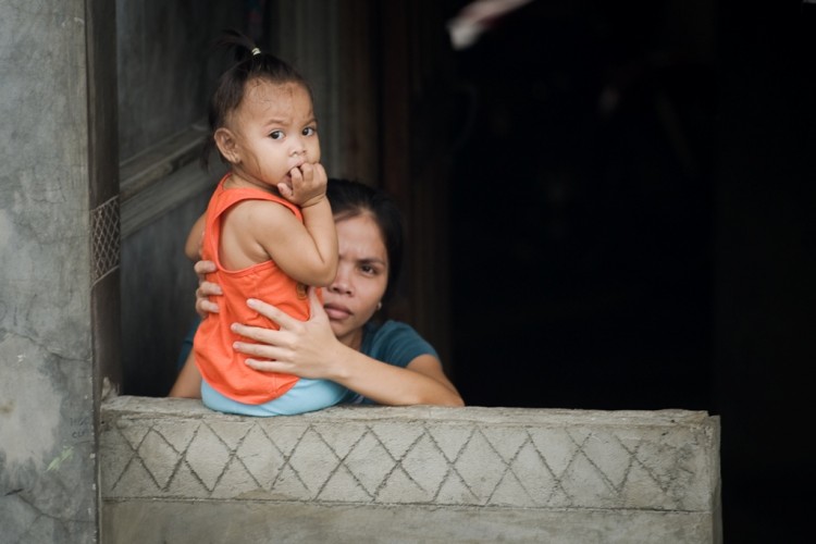 A woman supports a baby on a wall outside their home in Manila on Aug. 10. The Philippines high birth rate is correlated with widespread poverty. (Nicolas Asfouri/AFP/GettyImages)