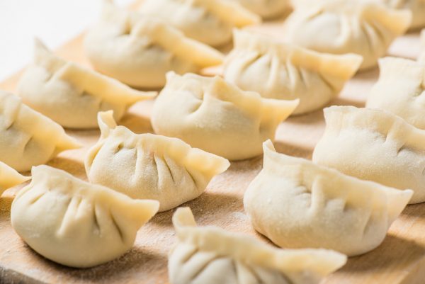 Raw homemade dumplings lined up on wooden board