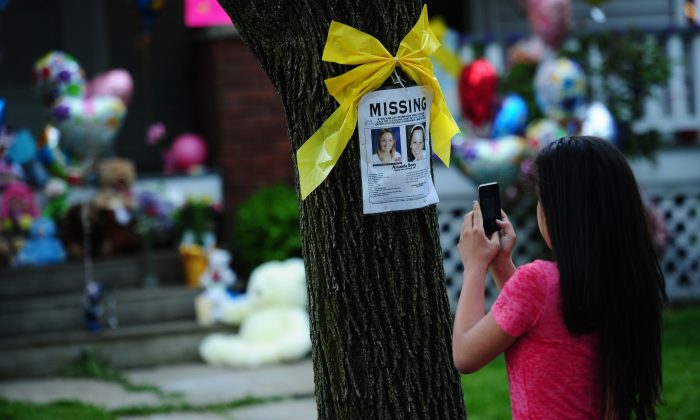 A girl takes a picture of a missing person sign displaying portraits of Amanda Berry, one of the three women held captive for a decade, in front of her sister's house in Cleveland, Ohio, on May 7, 2013. The three women were found safe, authorities said. (Emmanuel Dunand/AFP/Getty Images)