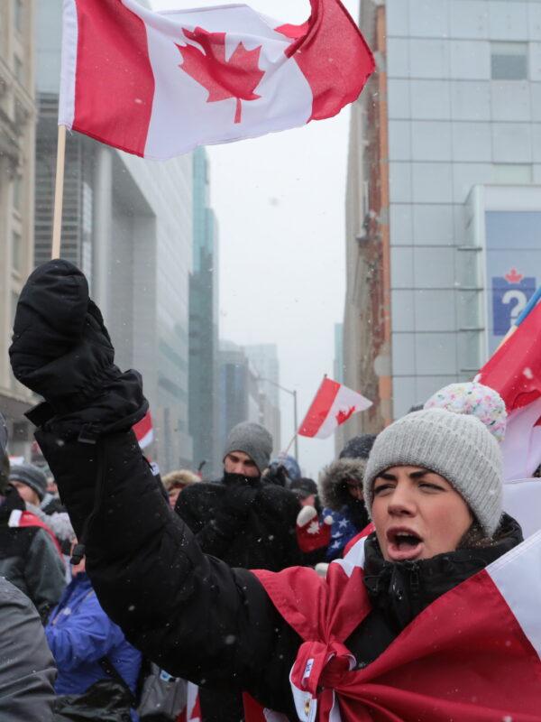 A protest supporter sings as she waves a Canadian flag at the heart of the truckers' camp on Wellington St., Ottawa, on Feb. 12, 2022. (Richard Moore/The Epoch Times)