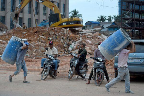 Cambodian men wait on motorcycles while two Chinese labourers work at a construction site in Sihanoukville, Cambodia, on Dec. 13, 2018. (Tang Chhin Sothy/AFP via Getty Images)