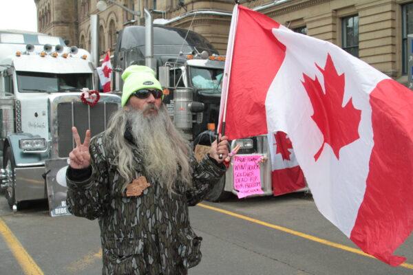 Protester Dana-Lee Melfi has a Canadian flag in one hand and makes a peace sign with the other at the site of the trucker protest in Ottawa on Feb. 12, 2022. (Richard Moore/The Epoch Times)