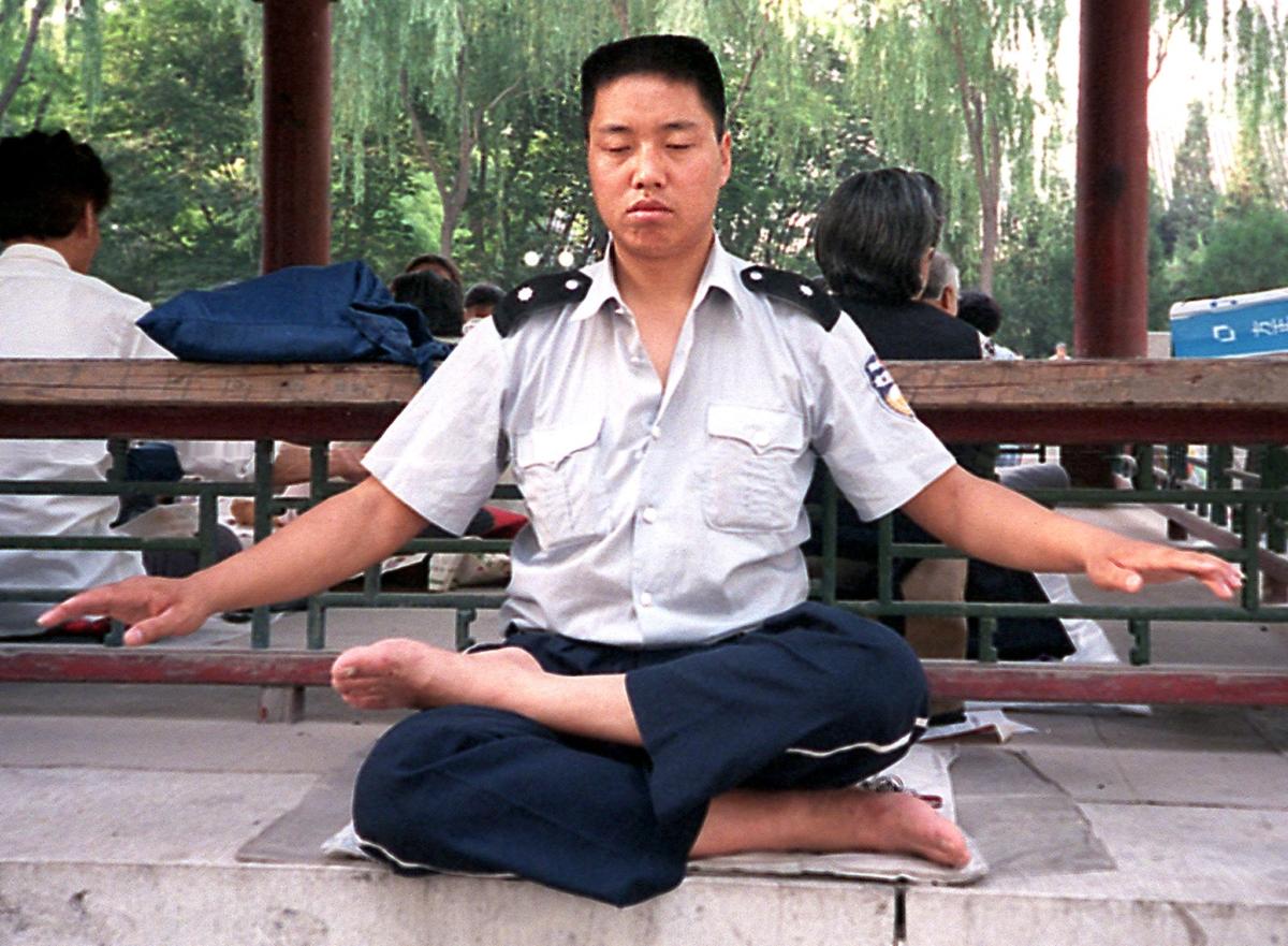 A Chinese public order enforcement officer practices the Falun Gong meditation together with other practitioners at a park in Beijing, on June 10, 1999. (Luisetta Mudie/AFP via Getty Images)