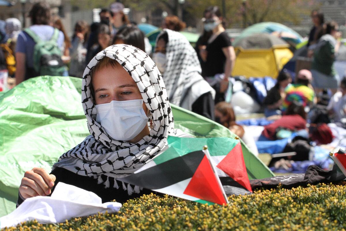 A protester stands by a hedge with Palestinian flags at the protest encampment on the Columbia University campus in New York City on April 23, 2024. (Richard Moore/The Epoch Times)