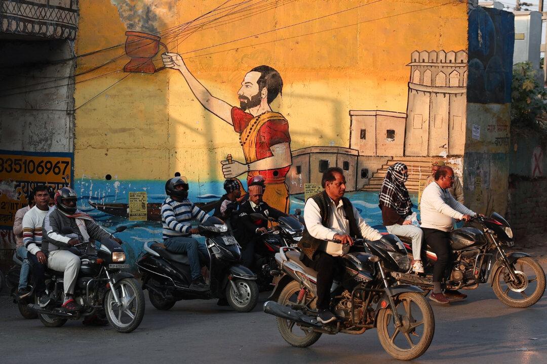 Motorists ride past a mural along a street in Varanasi on February 6, 2026. (Photo by Niharika KULKARNI / AFP via Getty Images)